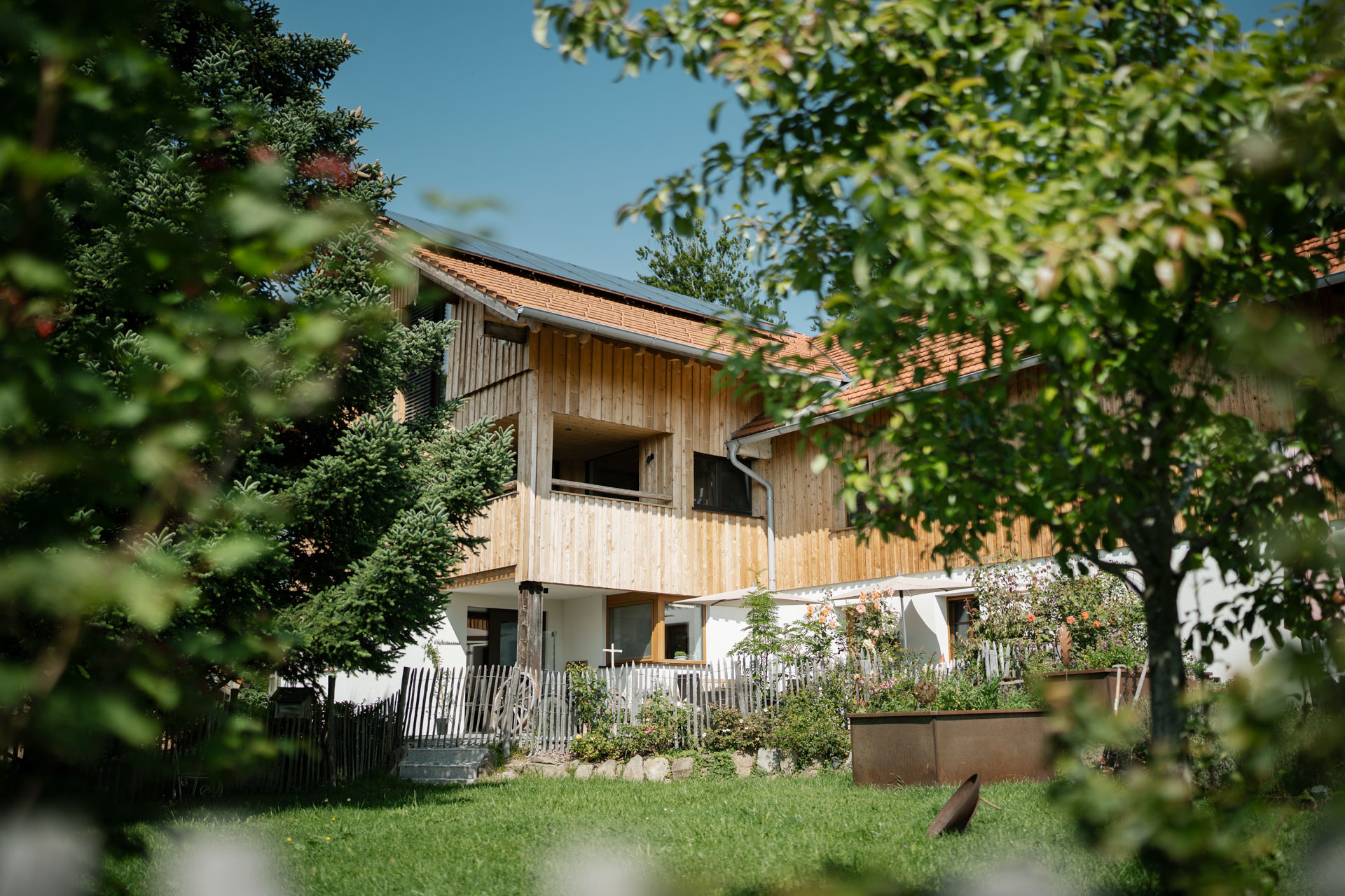 Außenansicht des Mächlerhofs mit Garten und Holzfassade.