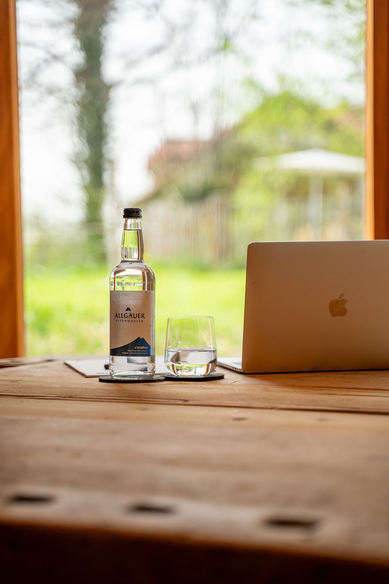 Arbeitsplatz in der Denkwerkstatt mit Wasserflasche, Glas und Laptop vor dem Fenster.